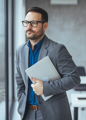 Professional Man in Suit Holding Laptop at Office Window