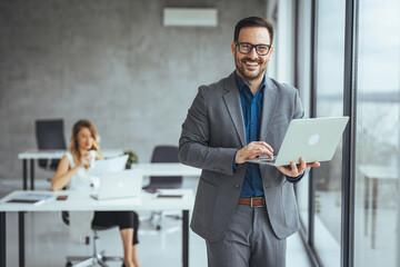 Professional Businessman Smiling While Working on a Laptop in a Modern Office