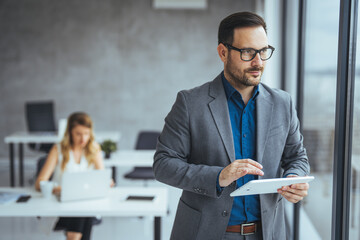 Confident Businessman Using Tablet in Modern Office with Colleague in Background