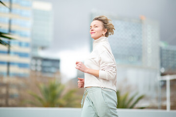 Confident middle aged blond woman running outdoors in urban environment
