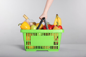 Woman with shopping basket full of products on gray background, closeup