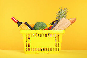 Shopping basket with different food products on yellow background