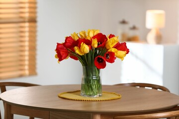 Beautiful tulips in vase on wooden table indoors