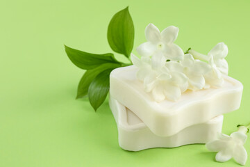Bars of soap and jasmine flowers on light green background, closeup. Space for text