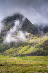 A truly serene view of misty Carrauntoohil mountain is complemented by lush green hills and soft clouds that gently envelop the majestic peaks, making it ideal for all nature lovers, Kerry, Ireland