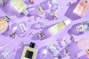 Flat lay composition with perfume bottles and lilac flowers on violet background