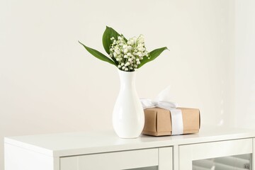 Beautiful lilies of the valley flowers and gift on white cabinet