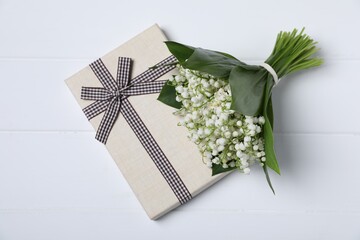 Bouquet of beautiful lily-of-the-valley flowers and gift on white wooden background, top view