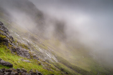 In a picturesque misty Carrauntoohil mountain scene, rolling fog envelops a lush green hillside, crafting a serene landscape that deeply inspires profound peace and tranquility, Kerry, Ireland