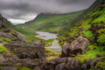 A breathtaking and stunning view of a vast mountainous landscape that showcases vibrant and lush greenery of Gap of Dunloe, with a tranquil lake nestled amongst the rocky terrain, Kerry, Ireland