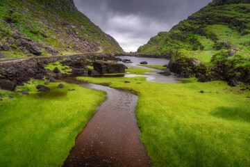 A serene river elegantly flows through a lush Gap of Dunloe, beautifully framed by rugged rocks and ominous stormy clouds, perfectly showcasing the splendid beauty of nature, Kerry, Ireland