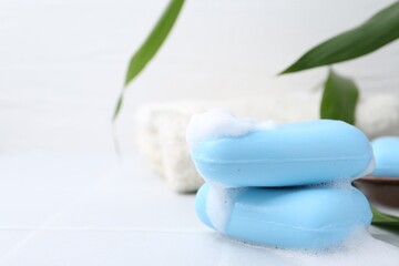 Soap bars with foam on white table, closeup. Space for text