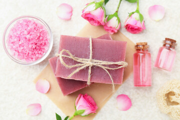Soap bars, sea salt, essential oils and beautiful roses on beige table, flat lay