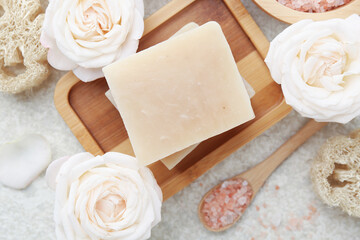 Soap bars, sea salt, loofah sponges and flowers on white textured table, flat lay
