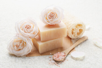 Soap bars, sea salt, loofah sponge and flowers on white textured table, closeup