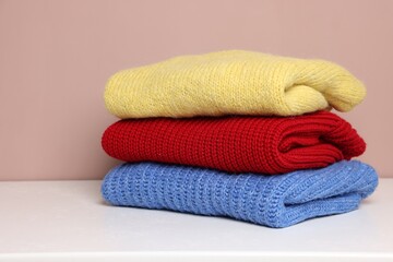 Stack of woolen sweaters on white table against color background, closeup