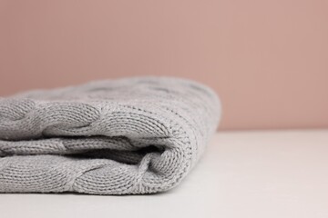 Folded woolen plaid on white table against color background, closeup. Space for text