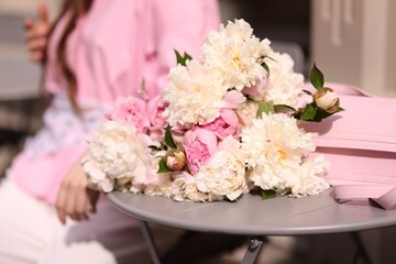 Stylish woman with beautiful peonies in outdoor cafe, closeup
