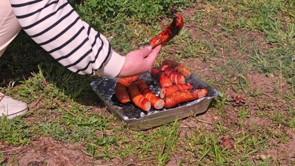 Caucasian Woman Cooking Tasty Fat Dripping Sausages Grilled on Disposable Single Use Portable Charcoal Grill