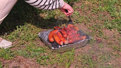 Caucasian Woman Cooking Tasty Fat Dripping Sausages Grilled on Disposable Single Use Portable Charcoal Grill