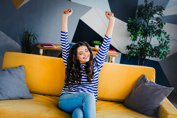 Pretty woman relaxing on a bright couch wearing a casual striped pullover in a modern and stylish...