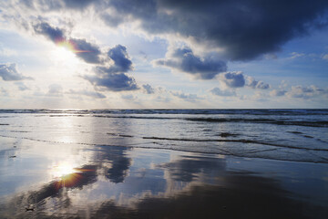 At sunset on the beach, the sun sets behind the clouds, reflecting vibrant colors over the sea on the coast, City of Donostia-San Sebastian.