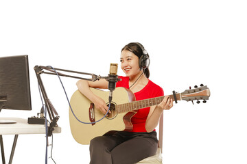 Beautiful Asian woman wearing headphones recording studio playing guitar