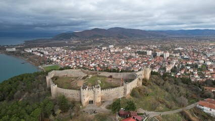 Historic Samuel's fortress overlooks serene coastal town with modern architecture under cloudy sky,...