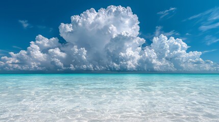 Large cloud is in the sky above a calm blue ocean. The sky is mostly clear, with only a few clouds scattered throughout. Scene is peaceful and serene, with the vast expanse of water
