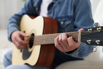 Man playing guitar on armchair indoors, closeup