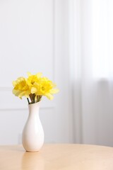 Beautiful daffodils in vase on wooden table at home. Space for text