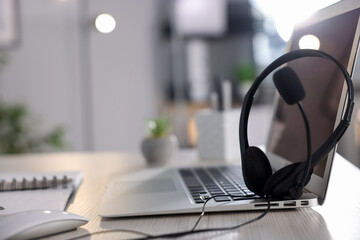 Headset with microphone and laptop on white wooden desk in office, closeup. Space for text
