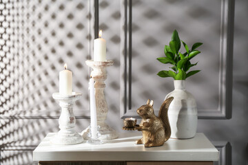 Elegant candlesticks with burning candles, branches in vase and other decor on dresser near grey...