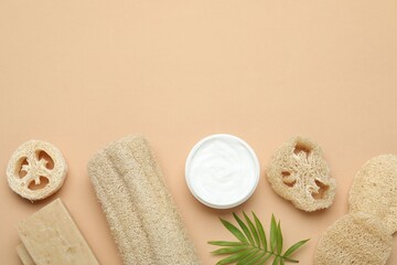 Loofah sponges, cosmetic product, soap and green twig on beige background, flat lay. Space for text