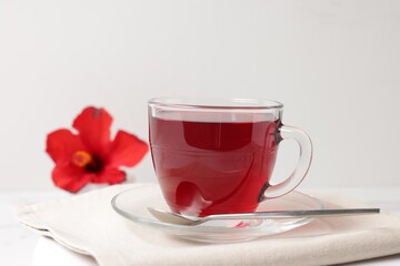 Delicious hibiscus tea in glass cup and spoon on white table, closeup