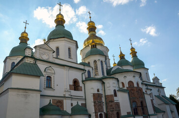 View of a grand historic cathedral featuring multiple green and golden domes topped with crosses, set against a partly cloudy blue sky. Saint Sophia Cathedral, Kyiv