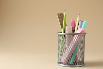 Different stationery in pen holder on beige background. Space for text