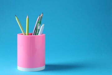 Pencils and pens in holder on light blue background