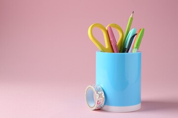 Different stationery in pen holder on pink background. Space for text