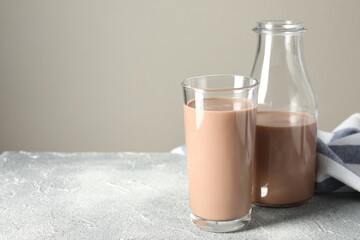 Tasty chocolate milk in glass and bottle on grey table, space for text