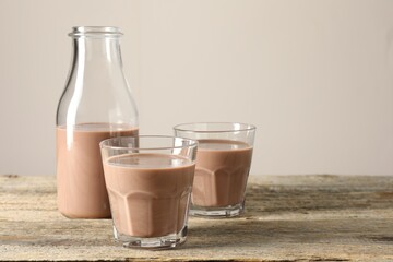 Tasty chocolate milk in glasses and bottle on wooden table, space for text