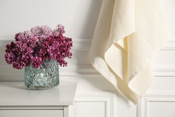 Clean waffle towels and vase of lilac flowers on white dresser in bathroom