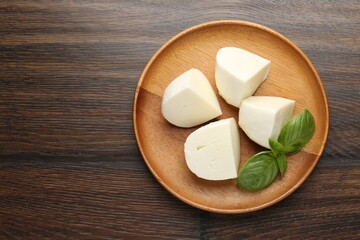 Pieces of delicious mozzarella cheese and basil on wooden table, top view. Space for text