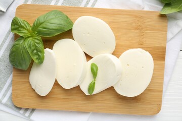 Pieces of delicious mozzarella cheese and basil on white wooden table, flat lay
