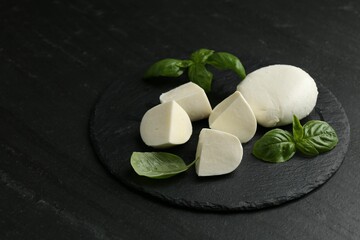 Pieces of delicious mozzarella cheese and basil on dark textured table, closeup