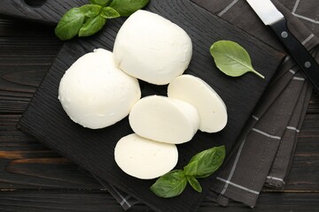 Pieces of delicious mozzarella cheese and basil on wooden table, flat lay