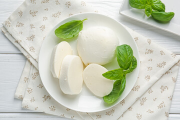 Pieces of delicious mozzarella cheese and basil on white wooden table, flat lay