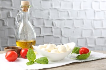 Tasty mozzarella cheese balls, tomatoes, basil and oil on wooden table