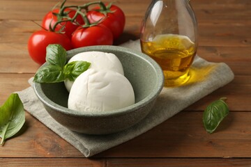 Tasty mozzarella balls, tomatoes and basil on wooden table, closeup