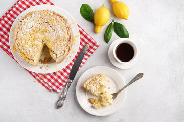 Homemade Italian lemon pie with streusel on light table with cut piece and cup of coffee, red napkin, top view, copy space